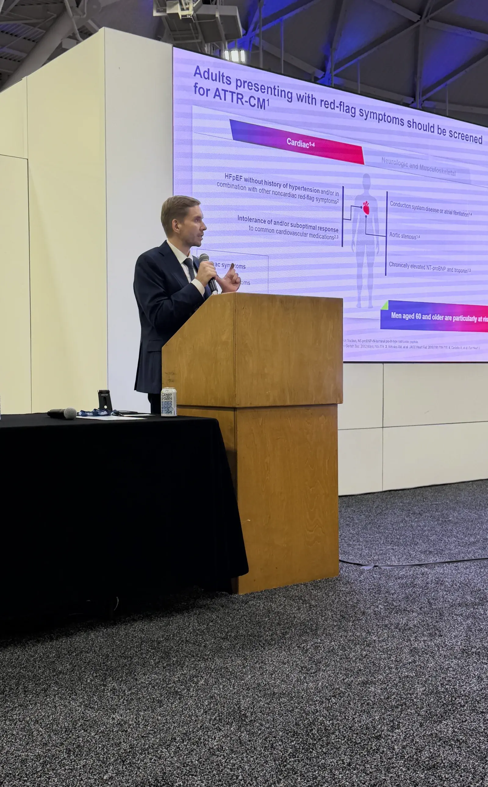 Dr. Yaranov speaking at a wooden lectern with a microphone, an ATTR-CM slide on the screen behind him