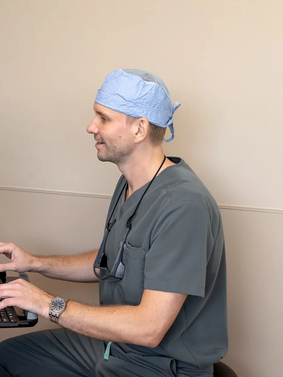 Dr. Yaranov in scrubs and a surgical cap, seated at a computer workstation