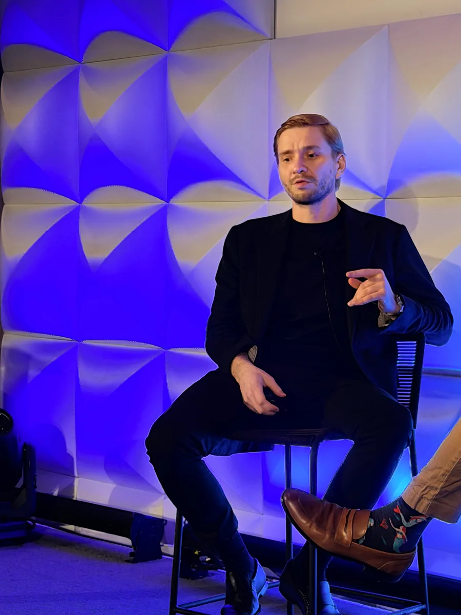 Dr. Yaranov seated on a stool, speaking and gesturing, in front of a blue lit wall