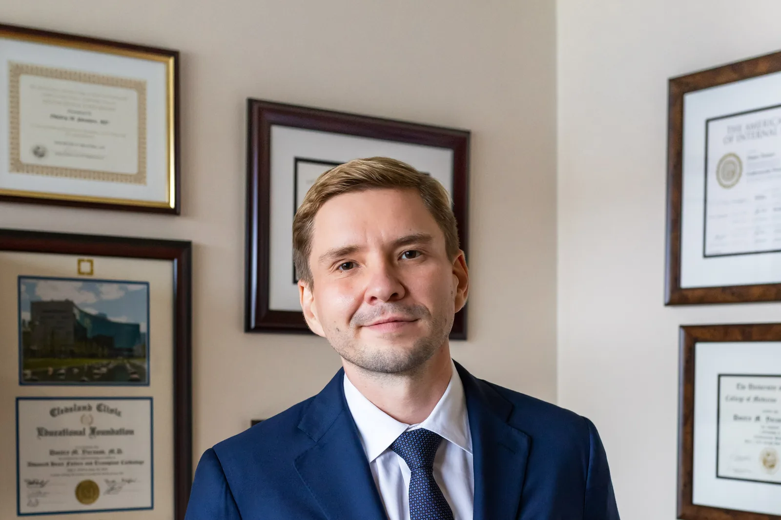 Dr. Yaranov in a navy suit in front of his framed diplomas